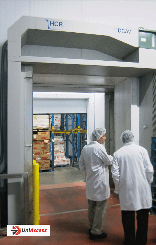 3 people in white coats and hair nets stand in front of an open metal doorway