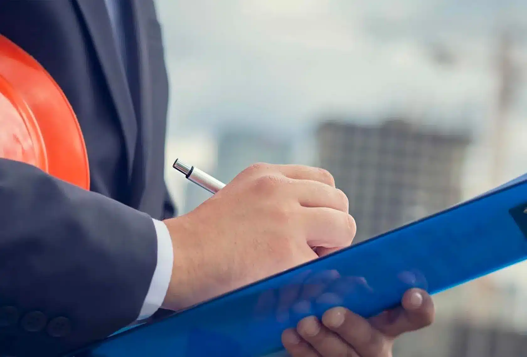 A person in a business suit, clutching a hardhat and writing on a blue clipboard.