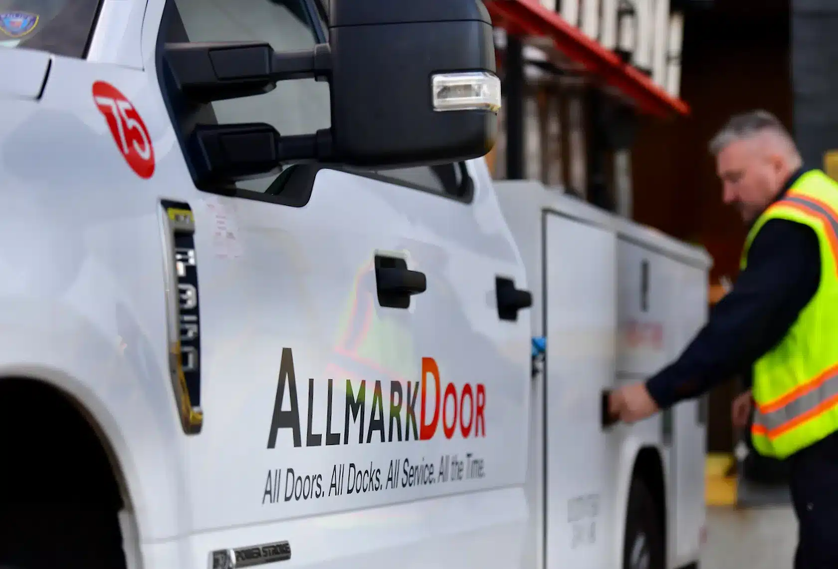 A man in a high-visibility vest at an Allmark Door truck.